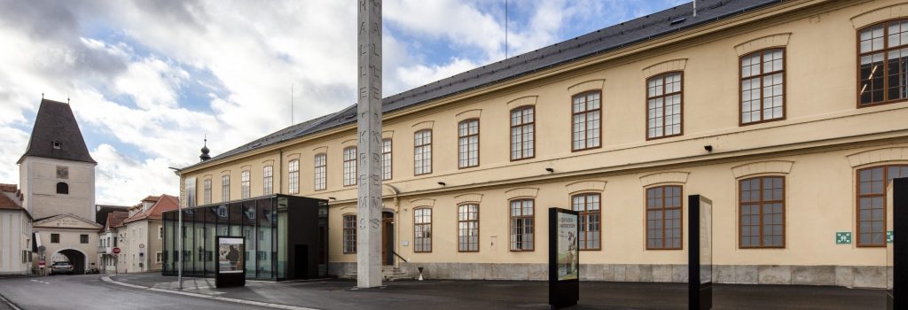 Auf dem Bild ist die Kunsthalle Krems von außen zu sehen. Der Himmel ist blau aber leicht bewölkt.