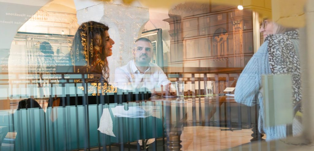 Wir starten mit einem Bild das unsere 4 Gesprächspartner für den Dialog durch eine Glasscheibe im museumkrems zeigt.