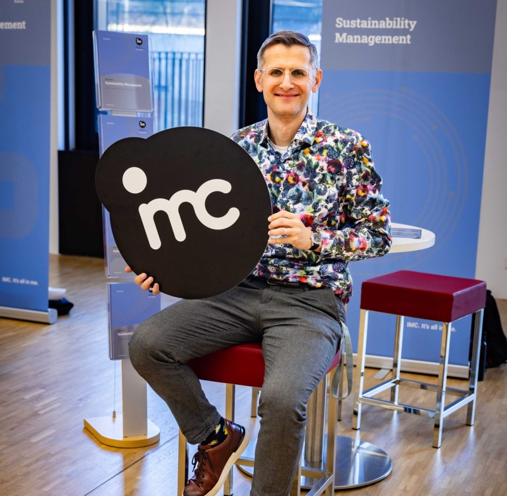 Auf dem Bild zu sehen ist Karl Michael Höferl mit einem Werbe-Schild des IMC Krems, wo er den Studiengang "Sustainability Management" leitet.