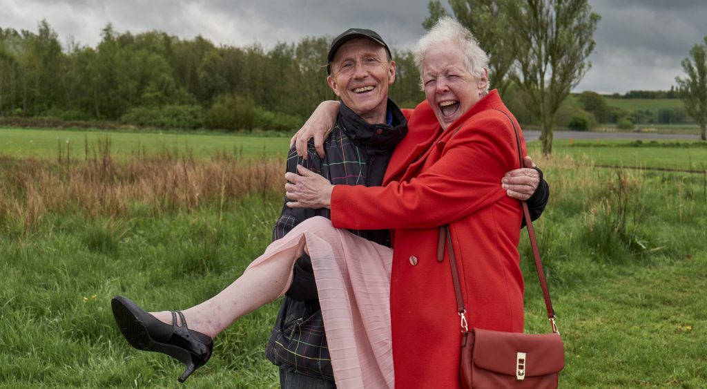 Portrait eines betagten Pärchens, bei dem der Mann die Frau auf seinen Händen trägt und sie herzhaft lacht. | Age-positive Image Library