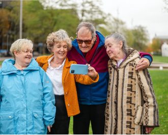 Vier ältere Menschen, die im Park ein Selfie von sich machen. | Foto: Peter Kindersley | Age-positive Image Library