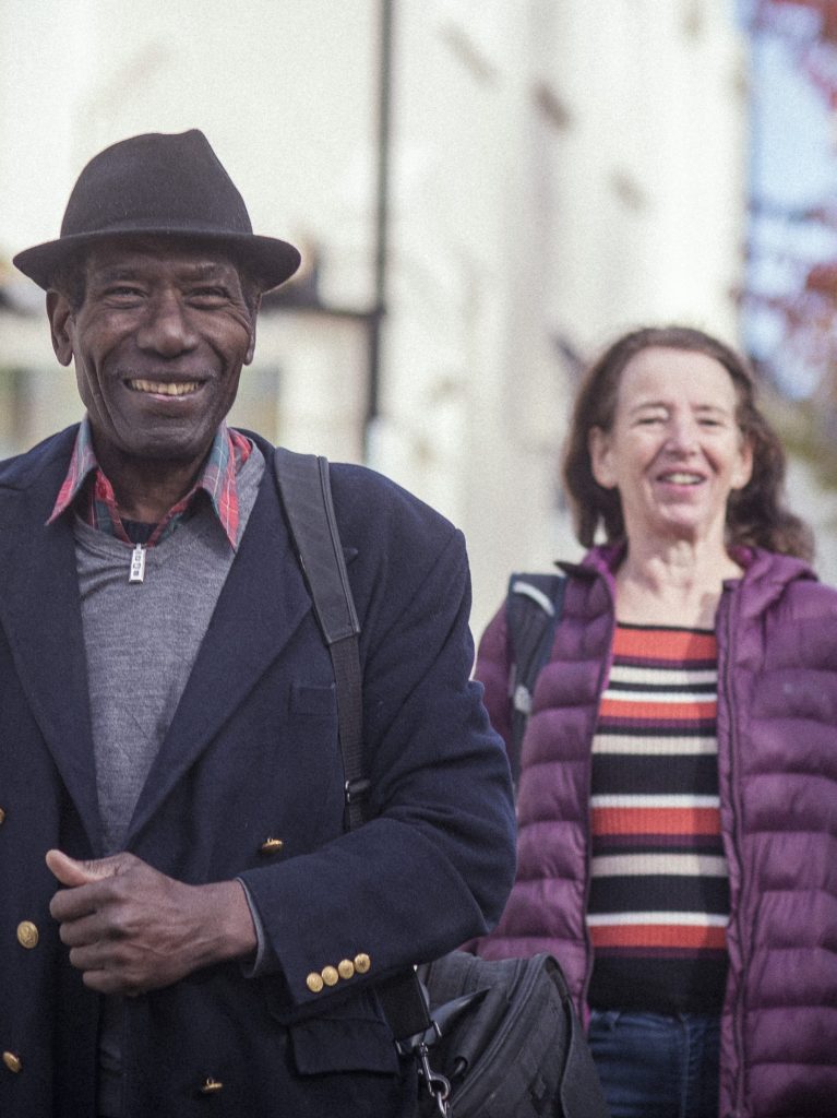 Zwei ältere Menschen, die lächelnd durch die Stadt gehen. | Foto: Peter Kindersley | Age-positive Image Library